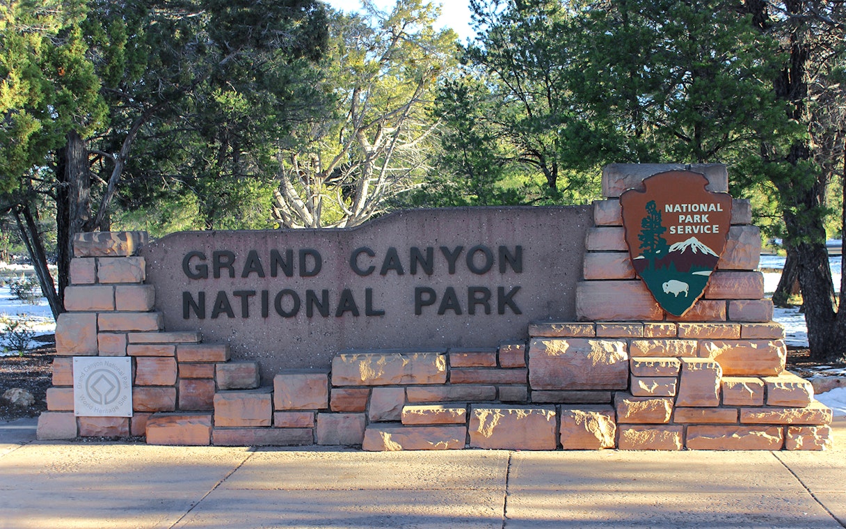 Grand Canyon National Park entrance sign surrounded by trees.