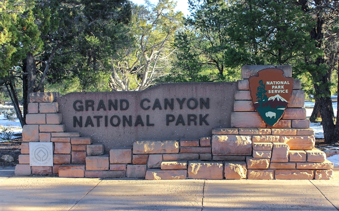 Grand Canyon National Park entrance sign surrounded by trees.