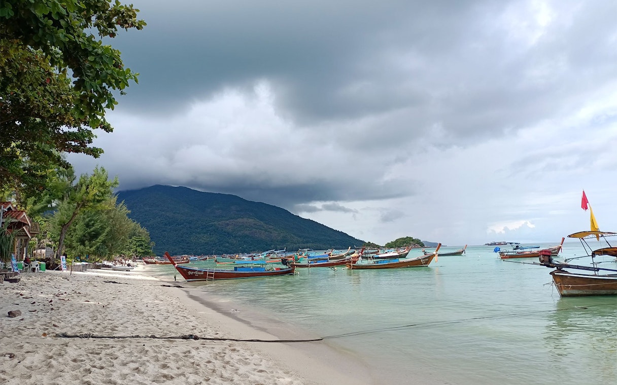 Boats anchored near the shore of Koh Lipe with lush hills in the background.