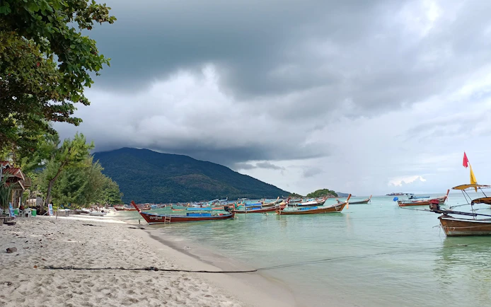 Boats anchored near the shore of Koh Lipe with lush hills in the background.