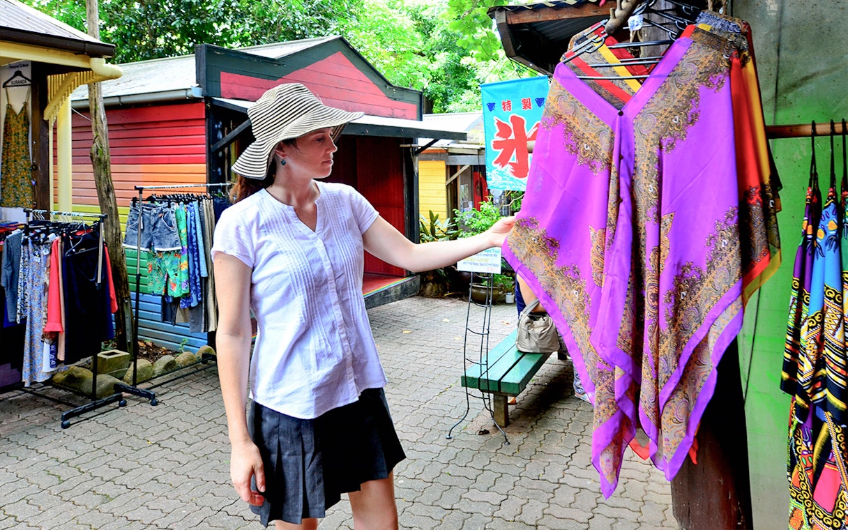 Woman shopping at Kuranda market, examining a colorful garment during the Full-Day Tour of Kuranda.