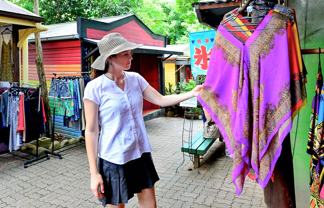 Woman shopping at Kuranda market, examining a colorful garment during the Full-Day Tour of Kuranda.