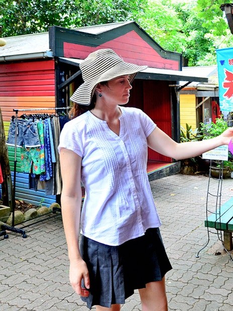 Woman shopping at Kuranda market, examining a colorful garment during the Full-Day Tour of Kuranda.