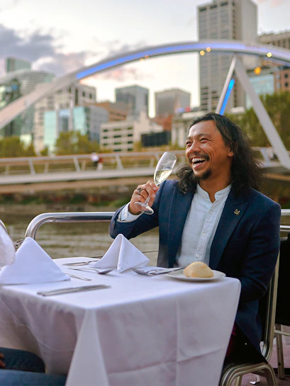 Man enjoying a glass of wine on a dinner cruise with Melbourne skyline in the background.