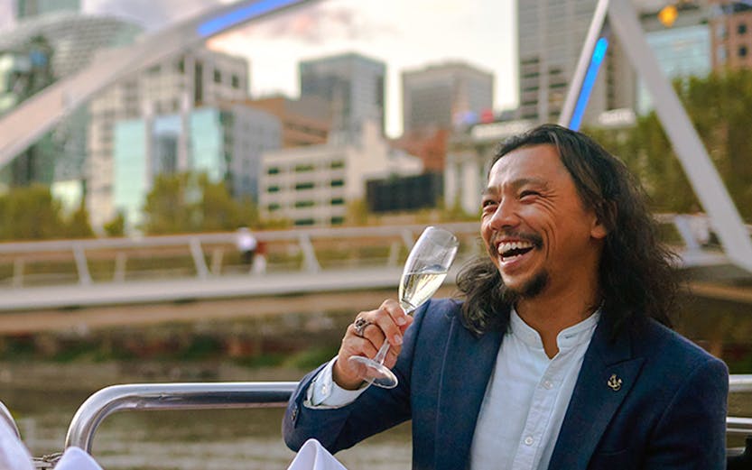 Man enjoying a glass of wine on a dinner cruise with Melbourne skyline in the background.