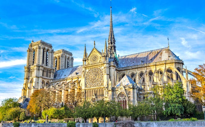 Notre-Dame Cathedral in Paris with detailed facade and spire under a blue sky.