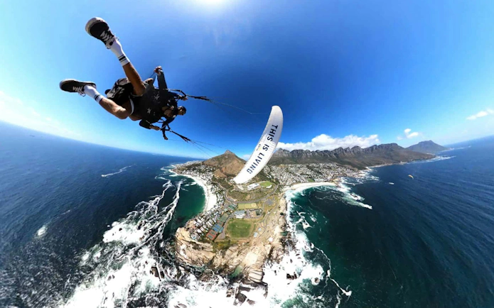 Tandem paragliding over Cape Town coastline with ocean and mountains in view.