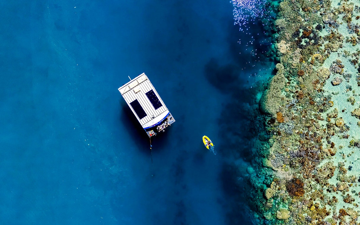 Glass bottom boat near coral reef at Airlie Beach, with a kayak nearby.