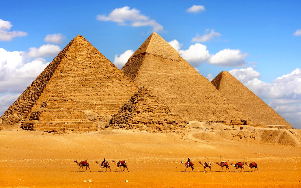 Pyramids of Giza with camels in the foreground under a blue sky.