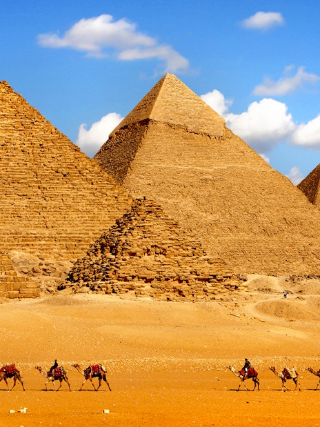 Pyramids of Giza with camels in the foreground under a blue sky.