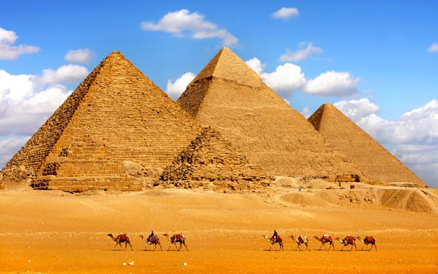 Pyramids of Giza with camels in the foreground under a blue sky.