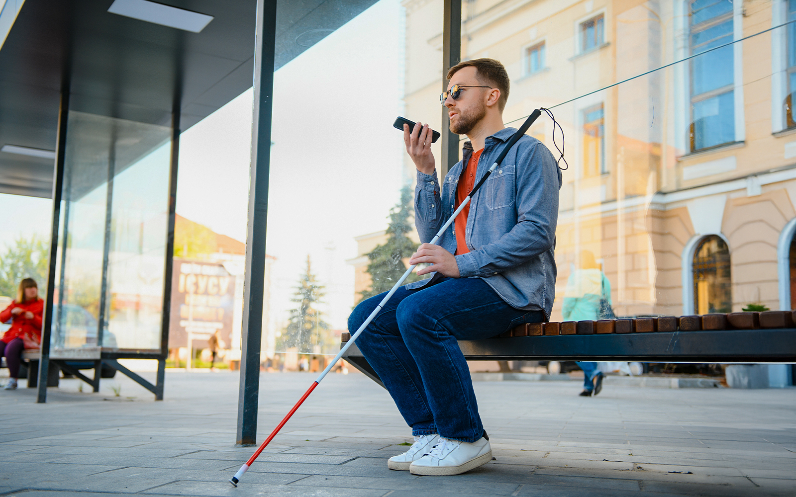 Blind man with walking stick and glasses sitting on a bench outside a museum.