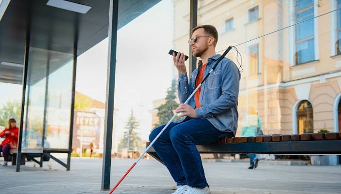 Blind man with walking stick and glasses sitting in a museum exhibit hall.
