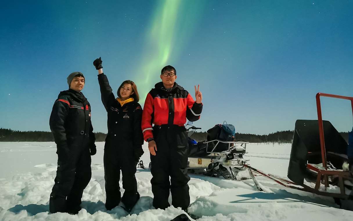 Group of friends on a snowmobile ride under Northern Lights in Levi, Finland.