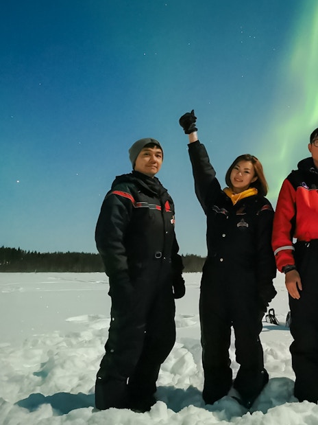 Group of friends on a snowmobile ride under Northern Lights in Levi, Finland.