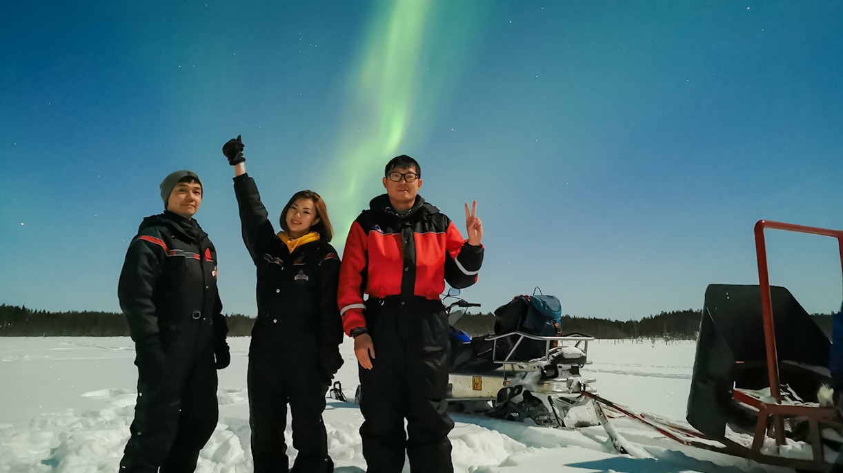 Group of friends on a snowmobile ride under Northern Lights in Levi, Finland.