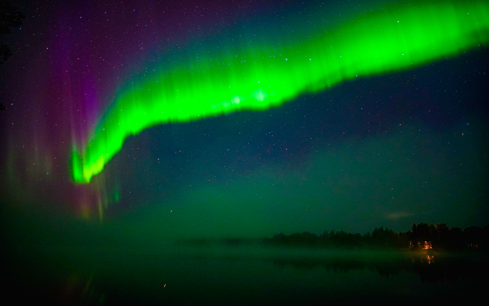 Northern Lights over a lake near Rovaniemi, Finland, with a forest silhouette.