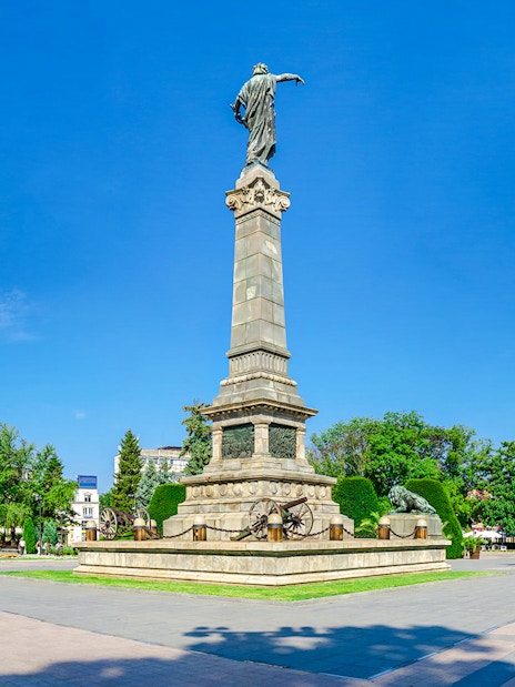 Freedom Monument in Ruse, Bulgaria, surrounded by trees and city buildings.