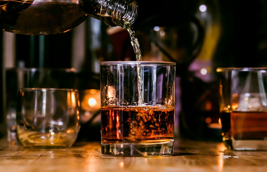 Pouring whiskey into a glass with dim lighting in the background.