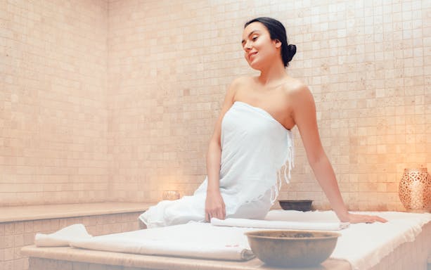 Woman relaxing in a Turkish hammam sauna, wrapped in a towel.