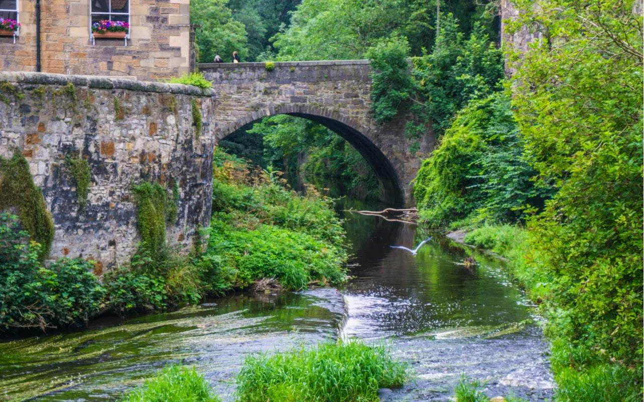 Stone bridge over a lush river in Edinburgh, part of the Romantic Edinburgh self-guided city exploration game.