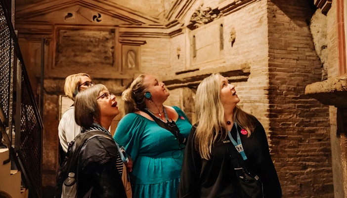 Tour group with audio guides exploring underground catacombs in Rome.