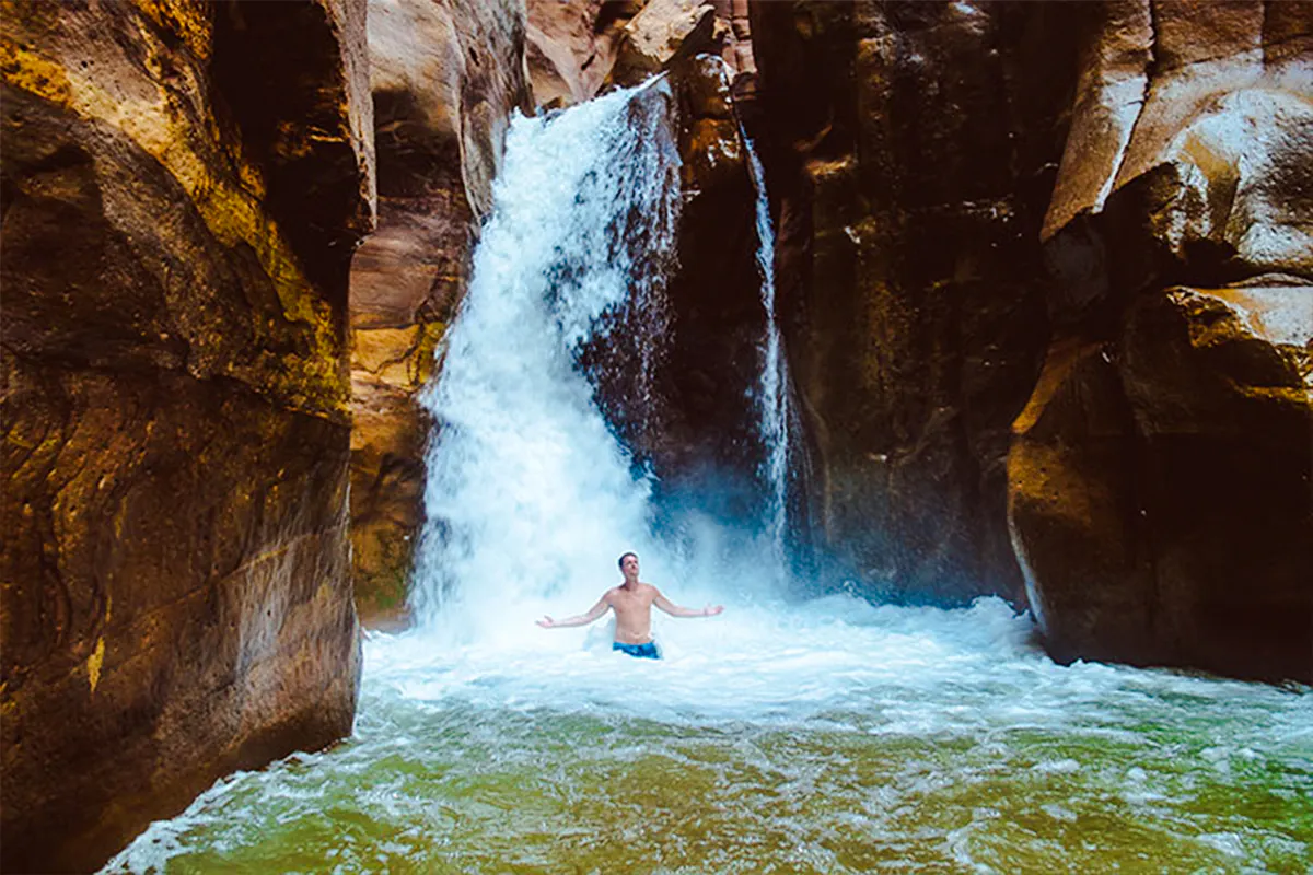 Person standing under waterfall in Wadi Mujib Siq Trail, Amman.