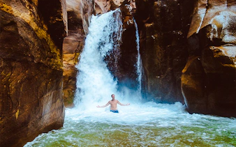 Person standing under waterfall in Wadi Mujib Siq Trail, Amman.