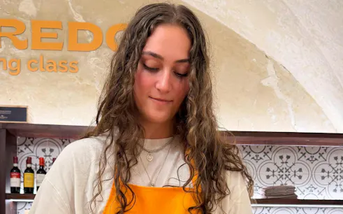 Person participating in a pasta-making class in Florence with wine bottles in the background.