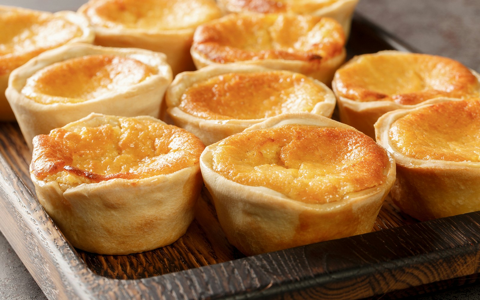 Queijadas de Sintra, sweet cheese tarts with cinnamon, on a wooden tray.