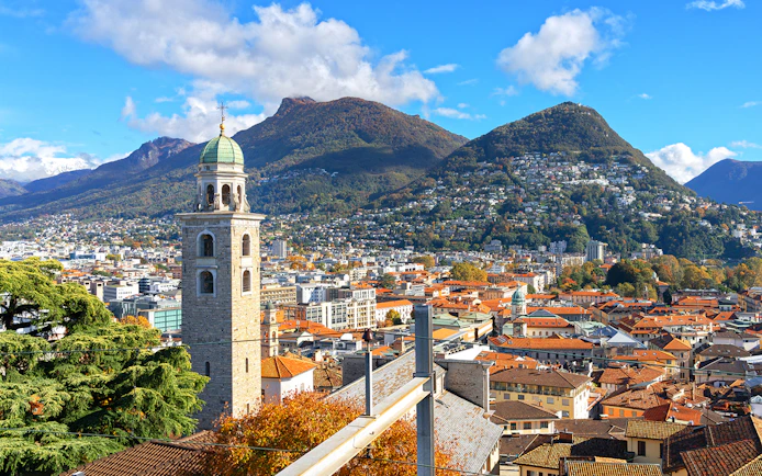 Panoramic view of Lugano with bell tower and mountains in the background.
