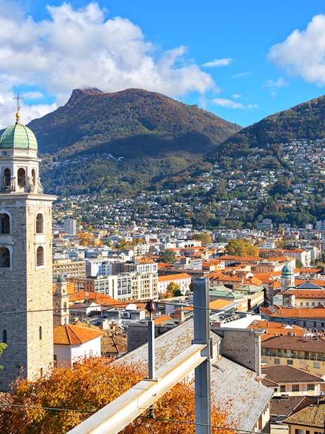 Panoramic view of Lugano with bell tower and mountains in the background.