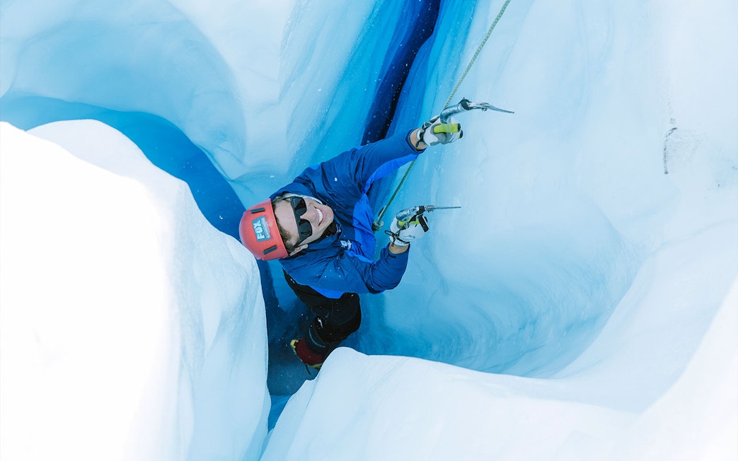Climber ascending icy crevasse during Fox Glacier heli hike in New Zealand.