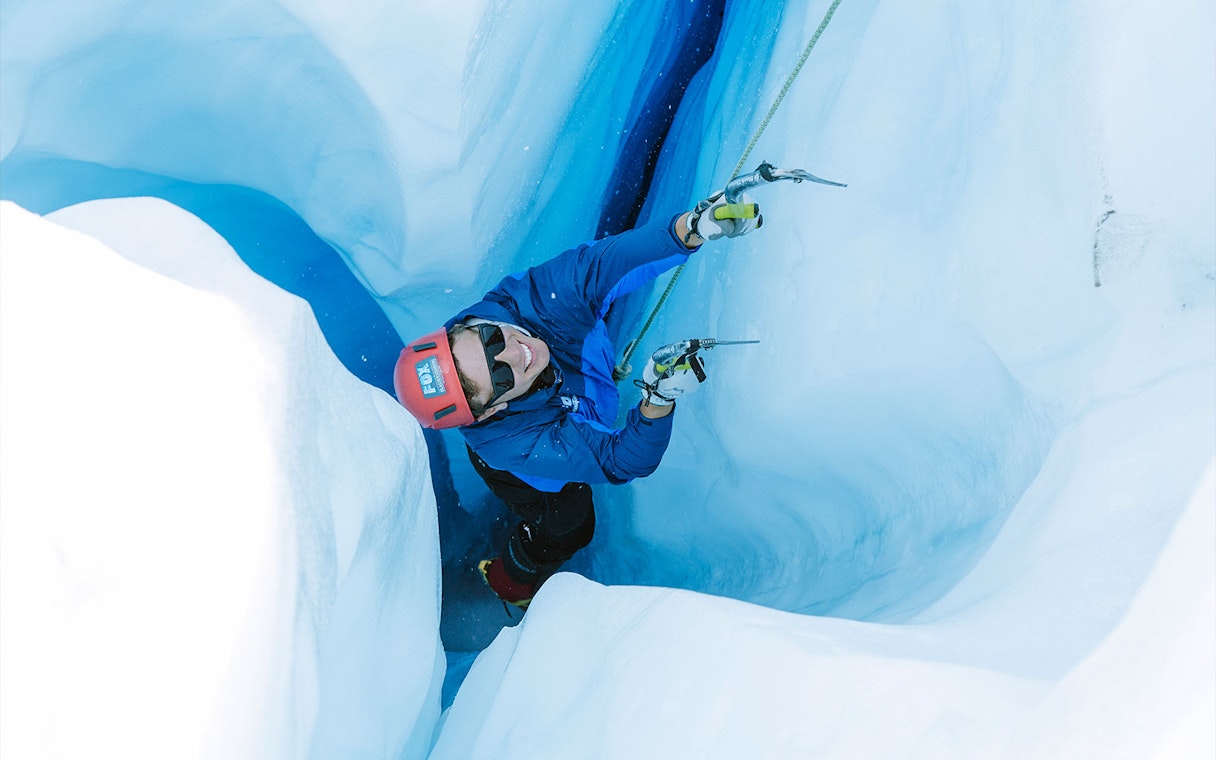 Climber ascending icy crevasse during Fox Glacier heli hike in New Zealand.