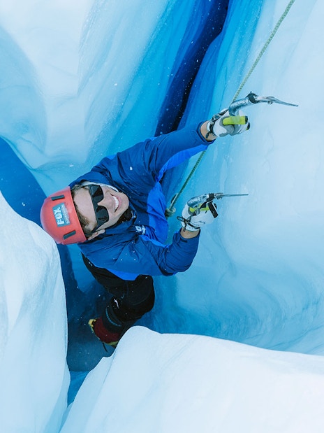 Climber ascending icy crevasse during Fox Glacier heli hike in New Zealand.