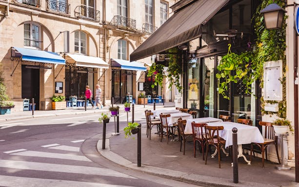 Parisian street with outdoor café tables and chairs, showcasing typical Paris architecture.