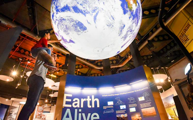 Child on adult's shoulders reaching for Earth exhibit at Science Centre Singapore.