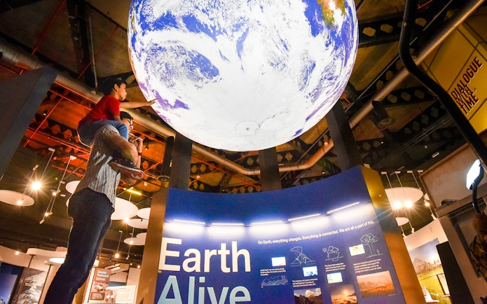 Child on adult's shoulders reaching for Earth exhibit at Science Centre Singapore.