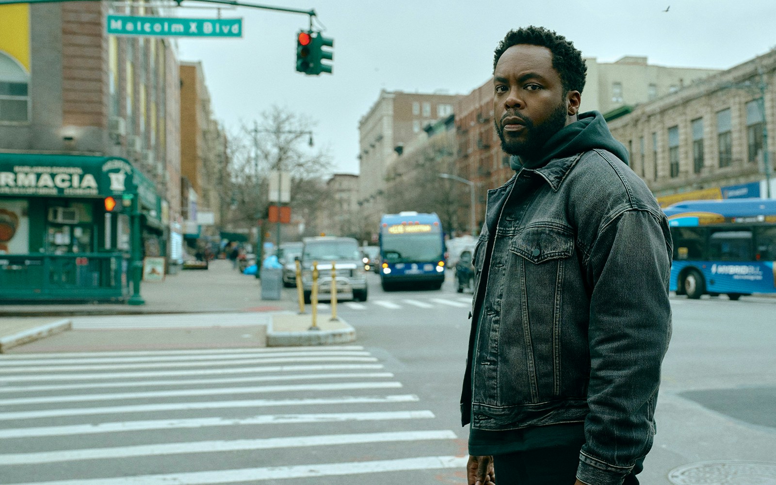 Man standing at Malcolm X Blvd intersection in an urban setting.