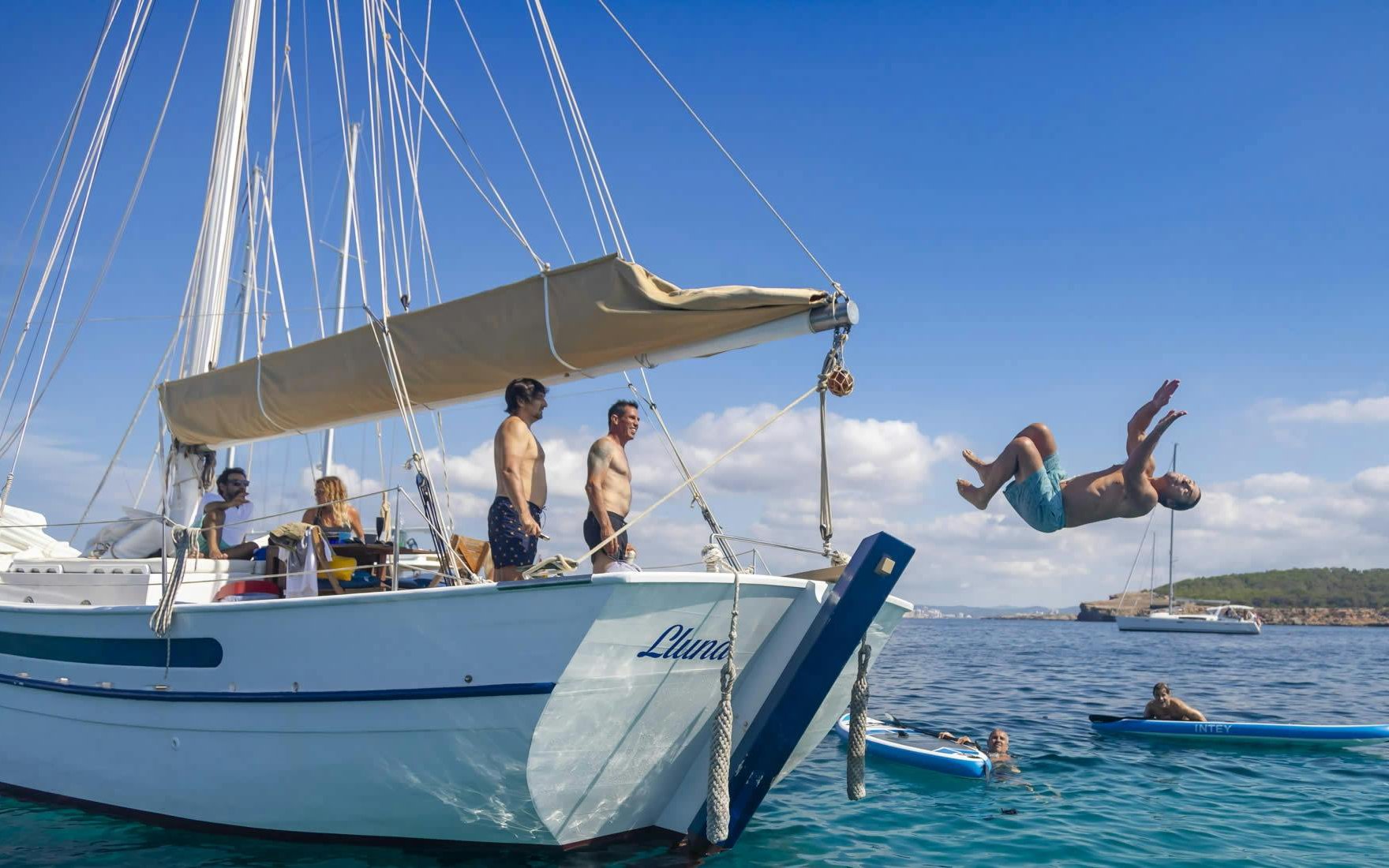 Tourists enjoying a private sunset cruise on a classic boat in Ibiza, with one person diving into the sea.