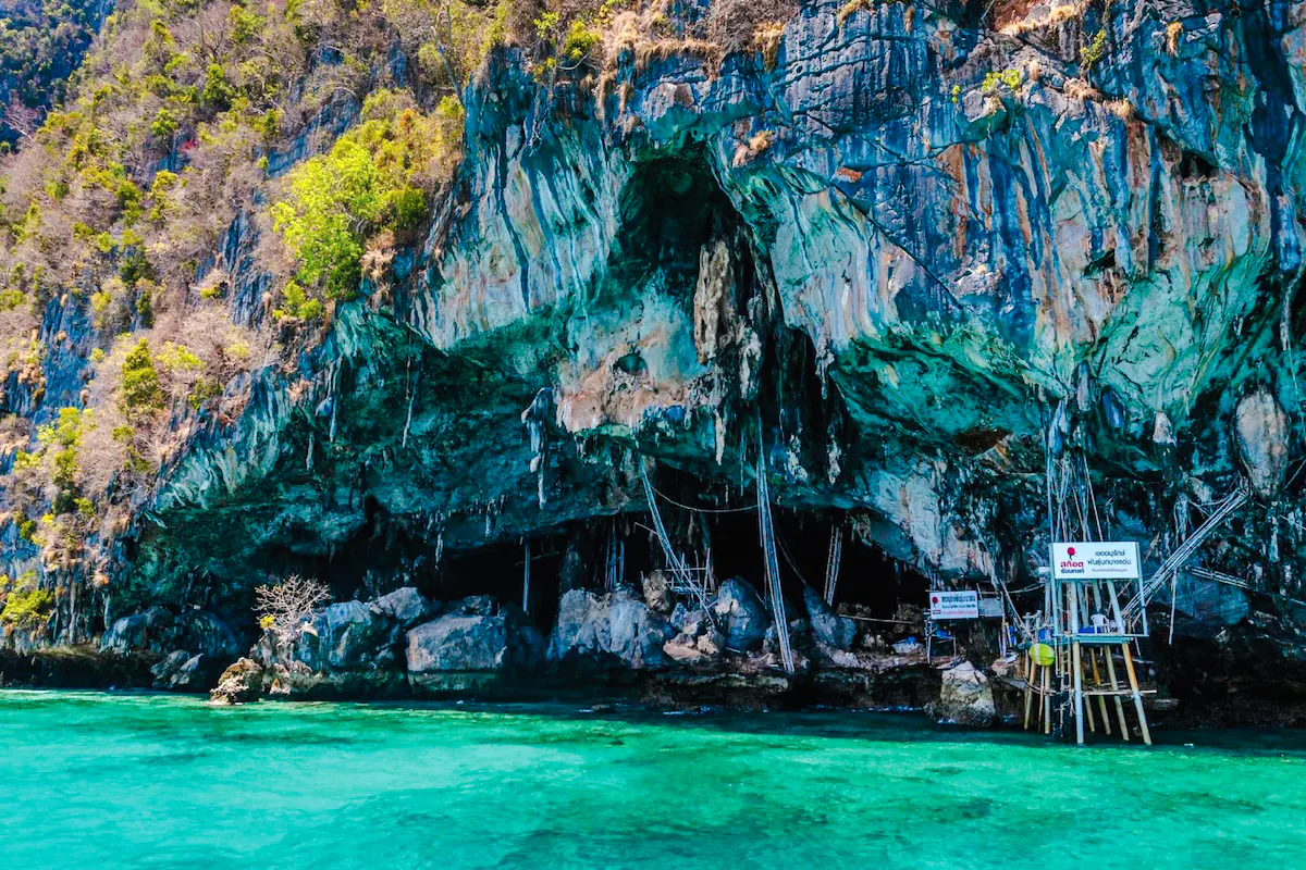 Rocky cliffside with vibrant greenery and clear turquoise water, Phi Phi ferry route, Phuket.