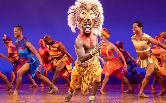 Performers in vibrant costumes dancing in The Lion King musical.