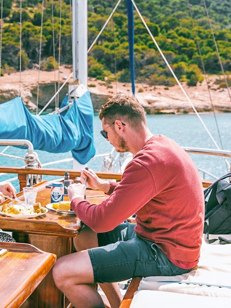 Couple enjoying lunch with beer on a cruise ship deck near a scenic coastline.