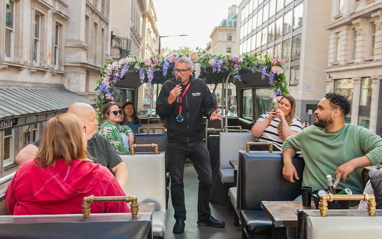 Guide speaking to tourists on a bar bus tour in London.
