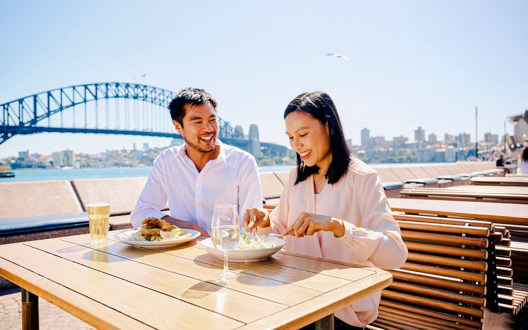 Couple dining outdoors with Sydney Harbour Bridge in the background.