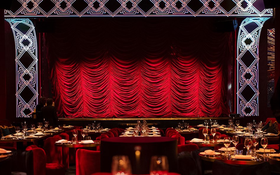 Stage with red curtains at Paris Paradis, tables set for dining.