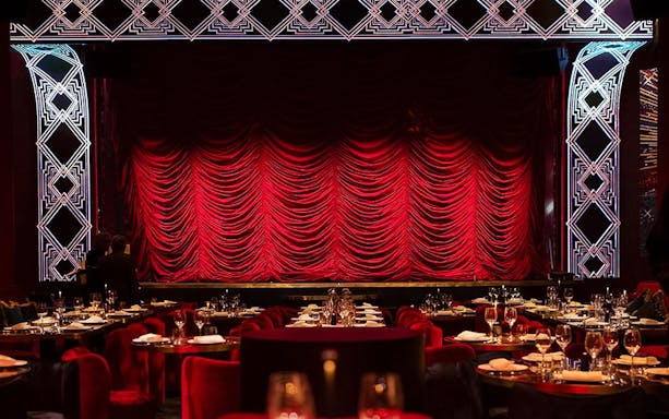 Stage with red curtains at Paris Paradis, tables set for dining.