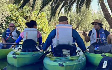 Kayakers with a local guide on a Xochimilco canal tour, surrounded by lush greenery.