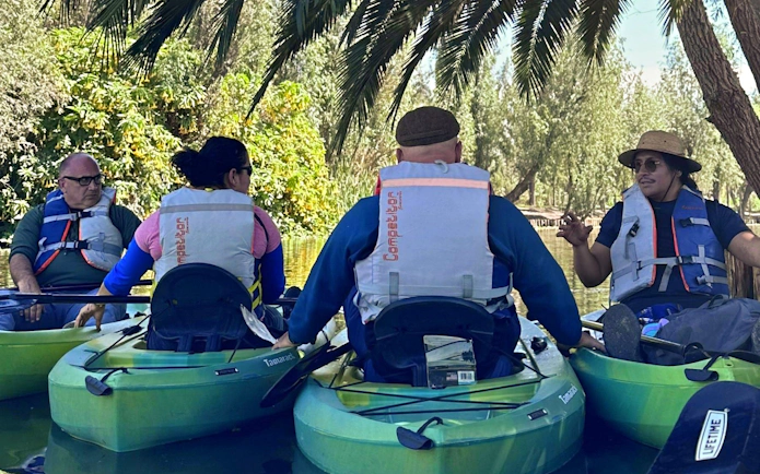 Kayakers with a local guide on a Xochimilco canal tour, surrounded by lush greenery.