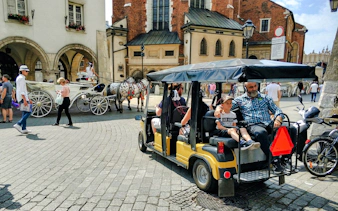 Golf cart tour in Krakow's Old Town with horse-drawn carriages and historic buildings in the background.